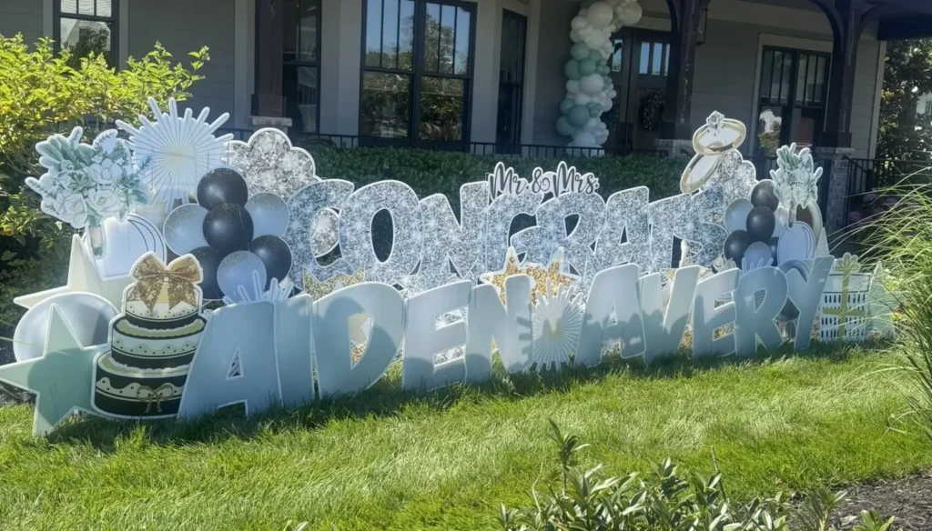 Custom "Congrats" wedding yard sign display with black, white, silver, and gold decorations, balloons, wedding cake, and ring graphics in a front yard.